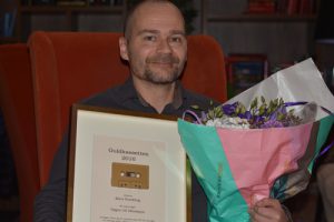 Vinnaren av Guldkassetten 2016, Mats Sundling, sitter leende i en röd fåtölj. I händerna håller han upp pristavlan, med en förgylld kassett, och en fin blomsterbukett.